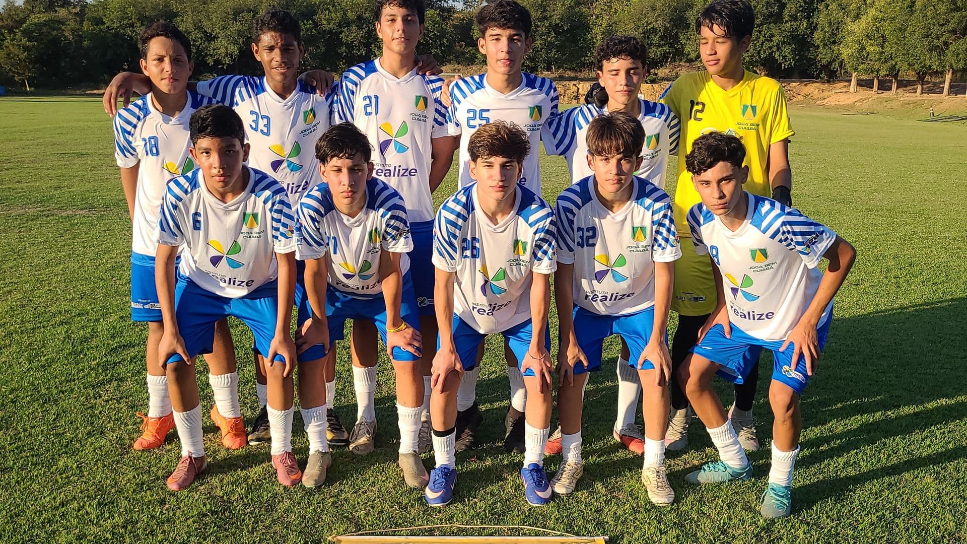 foto com alunos do projeto uniformizados em formação clássica em um campo de futebol gramado
